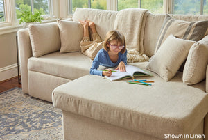 Child sitting on a beige sofa with a book and crayons, shown in linen finish.
